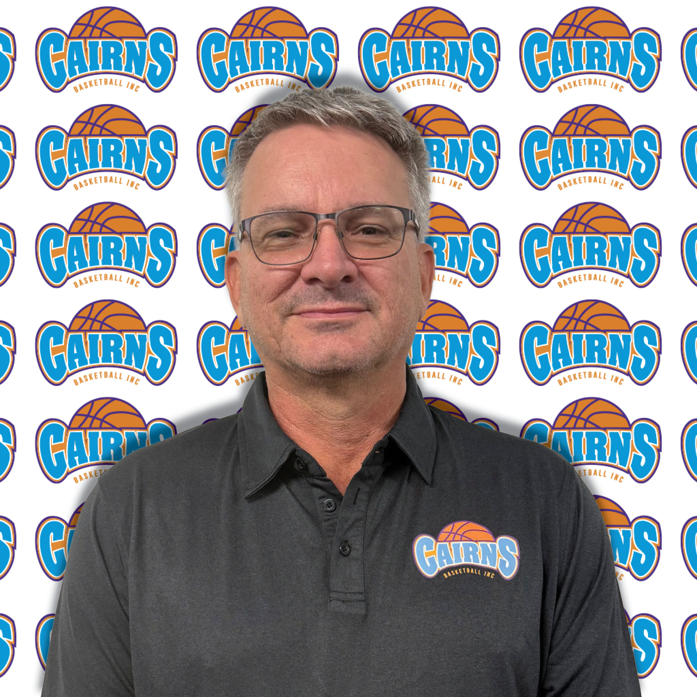 Close-up portrait of a man in a dark shirt wearing glasses, against a Cairns Basketball backdrop.