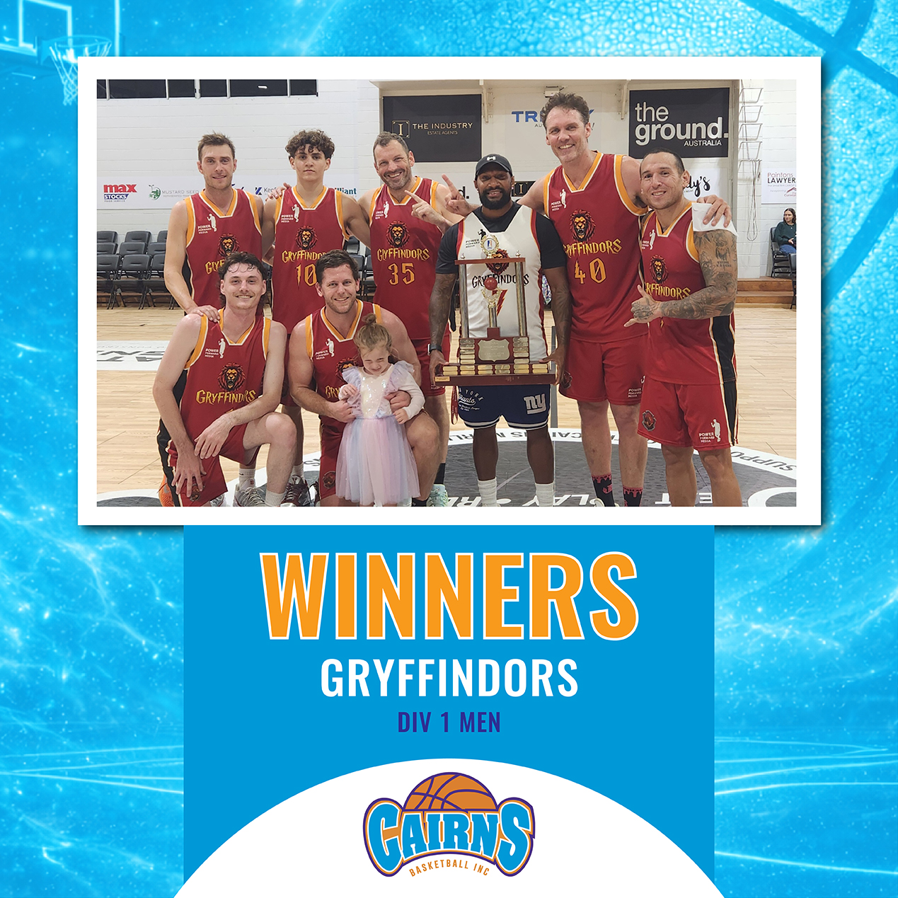 Gryfindors basketball team posing with a large trophy after winning Div 1 Men on a gym court, with a young girl in a white dress in front.