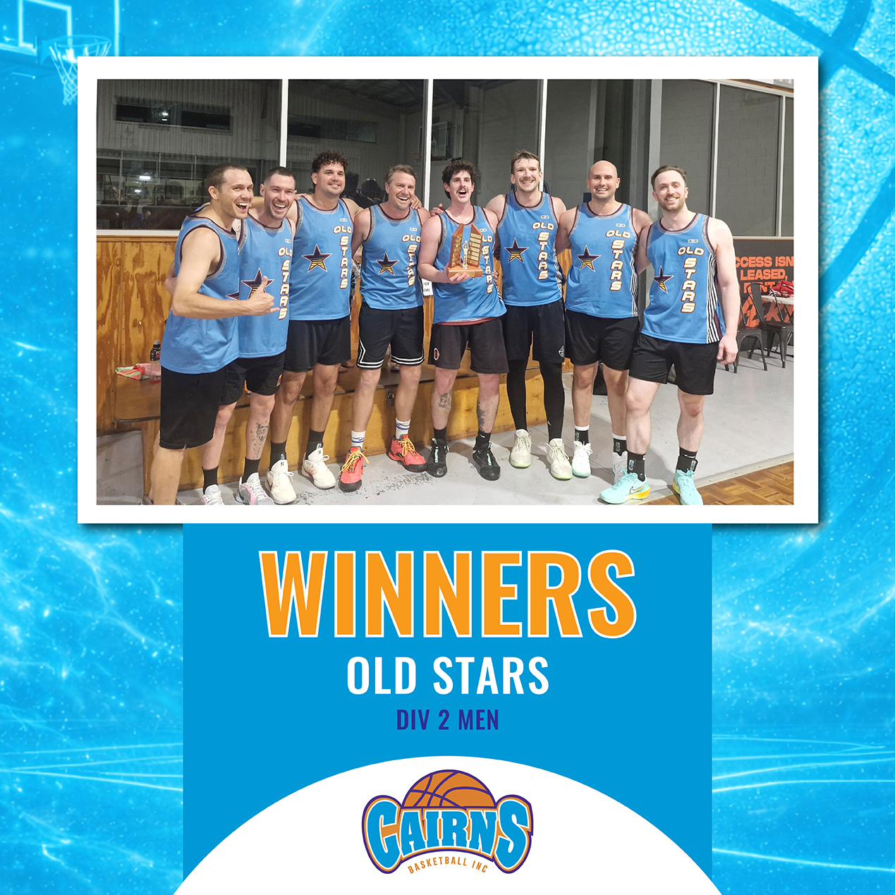 Group of men in blue Old Stars basketball jerseys pose with a trophy after winning, indoors on a court.